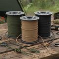 Spools of tactical paracord in olive green, black, and coyote tan on rugged wooden surface