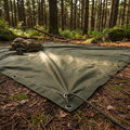 Heavy-duty military green tactical tarpaulin set up at a campsite with reinforced grommets and ropes